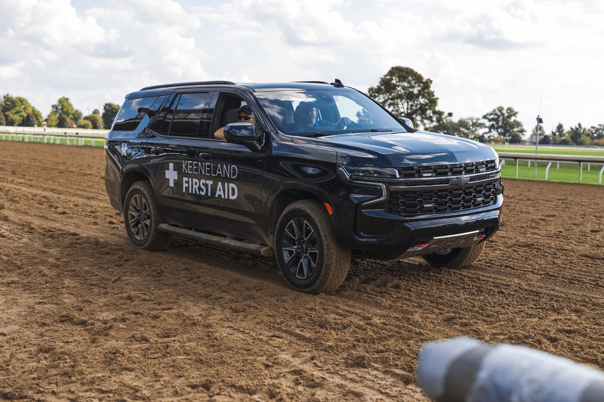 A picture of the Keenland First Aid car on the dirt track. It is a large black Chevy SUV.